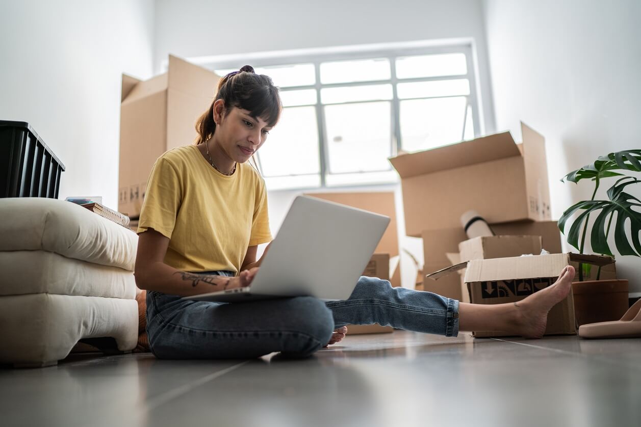 woman on laptop sitting floor moving boxes
